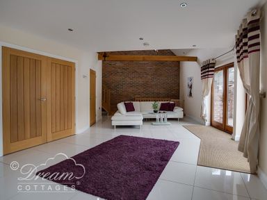 A living room with white sofa purple cushions purple rug wooden doors and brick wall at Baytree Lodge in Osmington