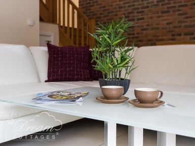 A glass coffee table with two brown cups and a plant in a pot in front of a white sofa with purple cushions at Baytree Lodge in Osmington