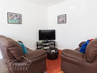 A living room with two brown leather sofas facing a television on a black stand with a gaming console and controller on a bean bag at Baytree Lodge in Osmington