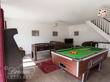 A game room with a pool table, foosball table, arcade machine, sofas, and a television at Baytree Lodge in Osmington