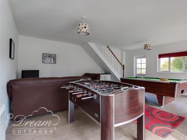 A game room with a foosball table, pool table, brown leather sofa, and staircase at Baytree Lodge in Osmington