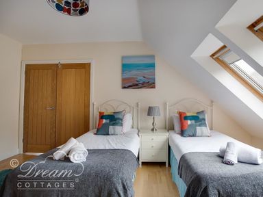 A bedroom with two single beds a nightstand with a lamp and a slanted window at Baytree Lodge in Osmington