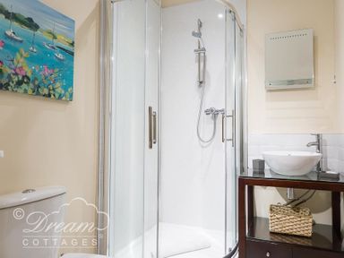 A bathroom with a glass shower enclosure a white sink on a wooden vanity and a toilet at Baytree Lodge in Osmington
