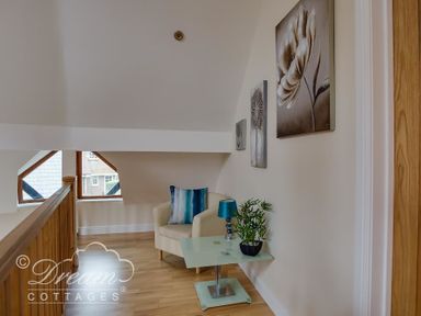 A small sitting area with an armchair a side table with a lamp and plant and artwork on the wall at Baytree Lodge in Osmington