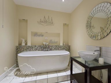 A bathroom with a freestanding bathtub and a sink with round mirror at Baytree Lodge in Osmington