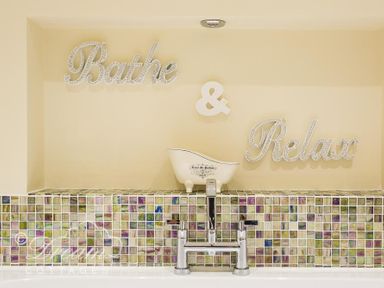 A bathroom wall with mosaic tiles and a bathtub faucet with decorative words Bathe and Relax on the wall at Baytree Lodge in Osmington