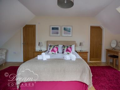A bedroom with a double bed with floral cushions bedside tables lamps two wooden doors and a dressing table at Baytree Lodge in Osmington