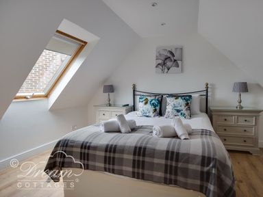 A bedroom with a bed with folded towels and cushions next to a skylight window and bedside tables with lamps at Baytree Lodge in Osmington