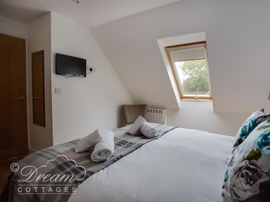A bedroom with a bed with rolled towels on it a wall-mounted television a chair and a skylight window at Baytree Lodge in Osmington