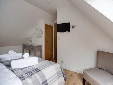 A bedroom with a bed covered with folded towels a chest of drawers with a mirror on the wall a mounted television and an upholstered chair at Baytree Lodge in Osmington