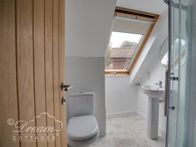 A bathroom with a wooden door toilet pedestal sink round mirror skylight window and a glass shower at Baytree Lodge in Osmington