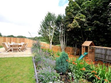 A garden with a wooden playhouse slide swings a flower bed and outdoor dining set at Baytree Lodge in Osmington