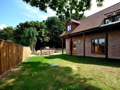 A backyard with a wooden fence green grass outdoor dining table and chairs next to a brick house at Baytree Lodge in Osmington