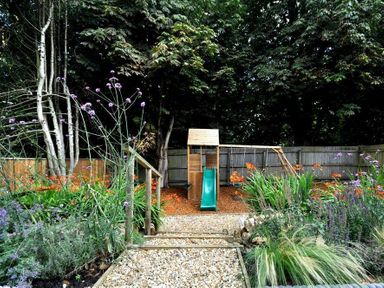 A garden with a children's playset including a slide and swings surrounded by plants and flowers at Baytree Lodge in Osmington