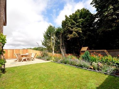 A backyard with a lawn wooden dining table and chairs flower beds and trees at Baytree Lodge in Osmington