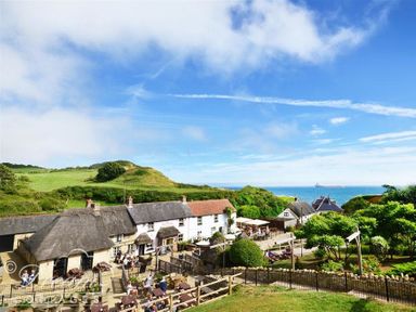 A coastal village with thatched roof cottages green hills and people sitting outside at Baytree Lodge in Osmington