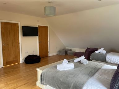 A bedroom with two beds with rolled towels a TV mounted on the wall two wooden doors a purple chair and storage baskets at Baytree Lodge in Osmington