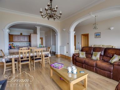 A living room with a brown leather sofa a wooden coffee table and a dining area with chairs and a table at Beach View Apartment 2 in Greenhill