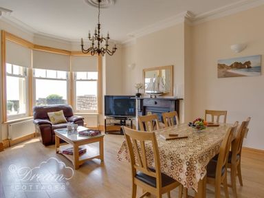 A living room with a dining table and chairs a sofa a coffee table a television and a fireplace at Beach View Apartment 2 in Greenhill