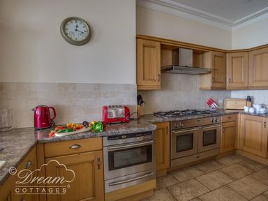 A kitchen with wooden cabinets a red kettle and toaster a wall clock and stainless steel ovens at Beach View Apartment 2 in Greenhill
