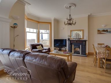 A living room with brown leather sofas a wooden coffee table a television above a fireplace and a dining table at Beach View Apartment 2 in Greenhill