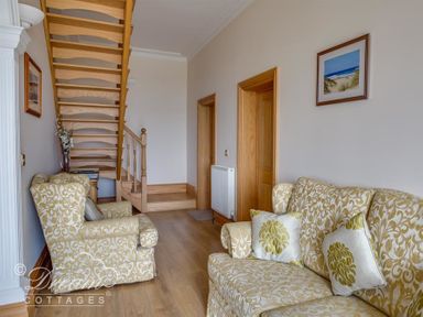 A sitting area with patterned sofas a wooden staircase and framed pictures on the walls at Beach View Apartment 2 in Greenhill