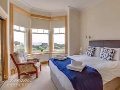 A bedroom with a double bed and armchair near bay windows overlooking a garden at Beach View Apartment 2 in Greenhill