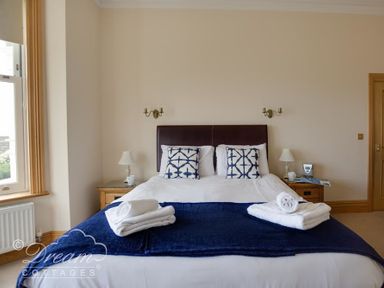 A bedroom with a double bed two bedside tables with lamps and windows with beige curtains at Beach View Apartment 2 in Greenhill