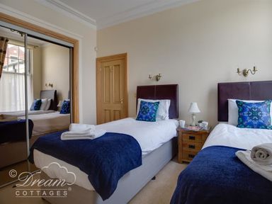A bedroom with two single beds a wooden nightstand and a mirrored wardrobe at Beach View Apartment 2 in Greenhill