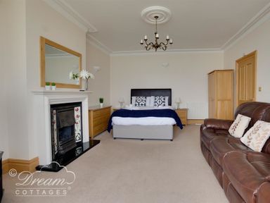 A bedroom with a bed a leather sofa a fireplace a wooden dresser and a wardrobe at Beach View Apartment 2 Greenhill