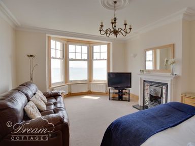 A living room with a leather sofa a television a fireplace and bay windows at Beach View Apartment 2 in Greenhill