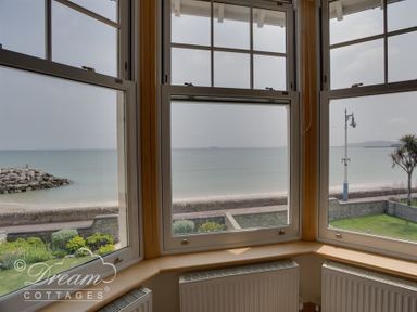 A bay window looking out onto a beach with a rock jetty and a streetlamp at Beach View Apartment 2 in Greenhill