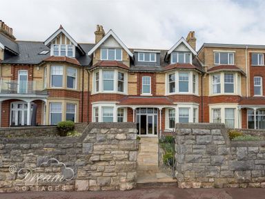 A row of brick and stone townhouses with bay windows and a stone wall with a metal gate in front at Beach View Apartment 2 in Greenhill
