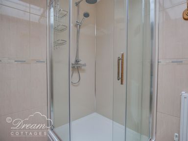 A shower enclosure with glass doors a rain shower head and a hand shower at Beach View Apartment 2 in Greenhill