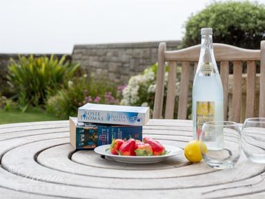 An outdoor wooden table with two books a plate of red peppers a bottle of cloudy lemonade a lemon and two empty glasses at Beach View Apartment 2 in Greenhill