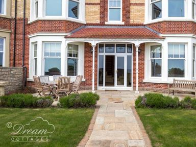 A front patio with a stone pathway wooden table chairs and bench outside a red brick house at Beach View Apartment 2 in Greenhill