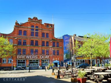 A red brick building with Brewers Quay sign and outdoor seating area with tables and trees at Beach View Apartment 2 in Greenhill