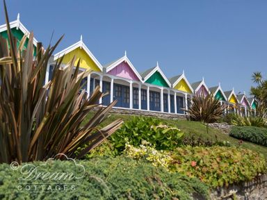 A row of cottages with colorful gable roofs and blue doors behind shrubs at Beach View Apartment 2 in Greenhill