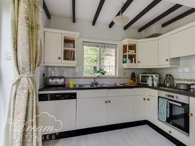 A kitchen with white cabinets black countertops a window above the sink and kitchen appliances at Little Berwick Cottage Burton Bradstock