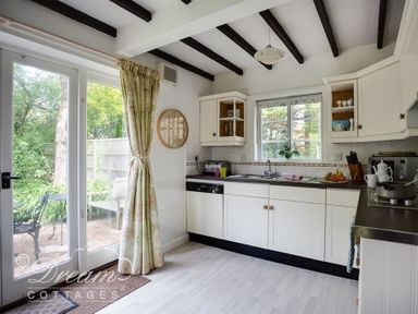 A kitchen with white cabinets a window over the sink and glass doors leading outside at Little Berwick Cottage in Burton Bradstock
