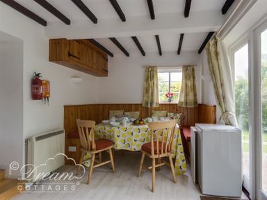 A dining area with a table covered with a yellow-patterned tablecloth surrounded by wooden chairs and built-in bench seating at Little Berwick Cottage in Burton Bradstock
