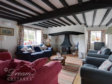 A living room with sofas around a wooden coffee table and a fireplace at Little Berwick Cottage in Burton Bradstock
