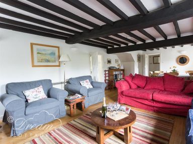 A living room with blue armchairs red sofa wooden coffee table and dining area at Little Berwick Cottage in Burton Bradstock