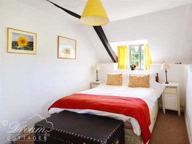 A bedroom with a double bed red throw cushions bedside tables and a window with yellow curtains at Little Berwick Cottage in Burton Bradstock