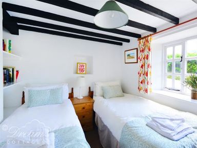 A bedroom with two single beds a wooden nightstand between and a window with floral curtains at Little Berwick Cottage in Burton Bradstock