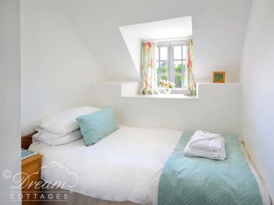 A small bedroom with a single bed next to a window with floral curtains at Little Berwick Cottage in Burton Bradstock