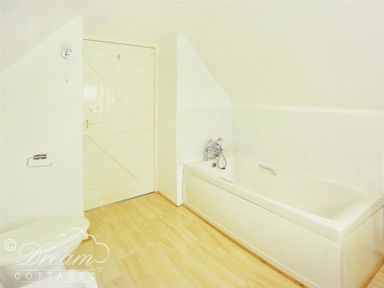 A bathroom with a bathtub a toilet and a wooden door at Little Berwick Cottage in Burton Bradstock