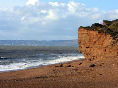 A beach with a large cliff on the right and waves from the sea at Little Berwick Cottage in Burton Bradstock