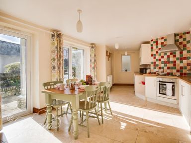 A kitchen with a dining table and chairs next to large windows and tiled backsplash at Blueberry Cottage in Sutton Poyntz