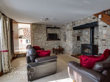 A living room with stone walls leather sofas red cushions a wood burning stove and a doorway leading to a kitchen at Blueberry Cottage in Sutton Poyntz